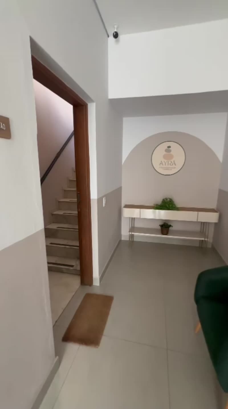 Recepção do prédio com aparador, plantas e poltrona verde